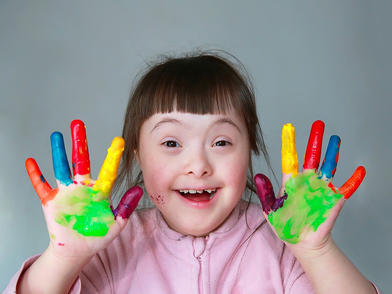 Verstandelijk beperkt meisje dat haar handen laat zien, die met kleurrijke verf bedekt zijn.