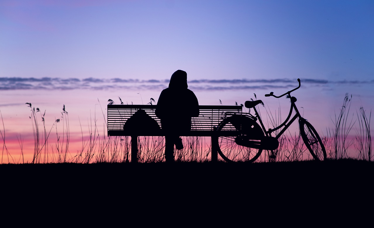 eenzaamheid Iemand zit alleen op een bankje in het donker met fiets naast zich
