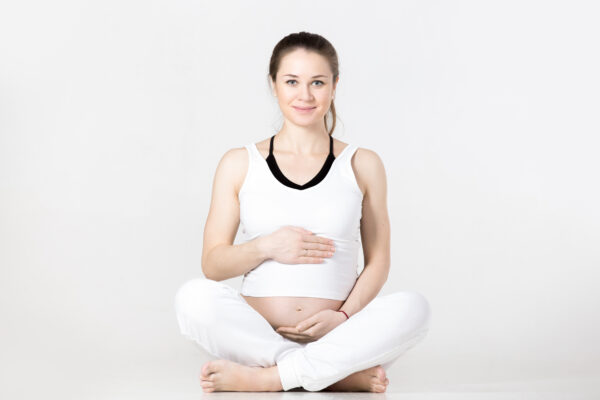 zwangere vrouw in wit sportpak in kleermakerszit