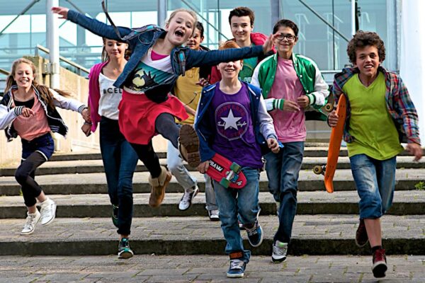 groepje van acht blije kinderen met skateboards komen aanrennen