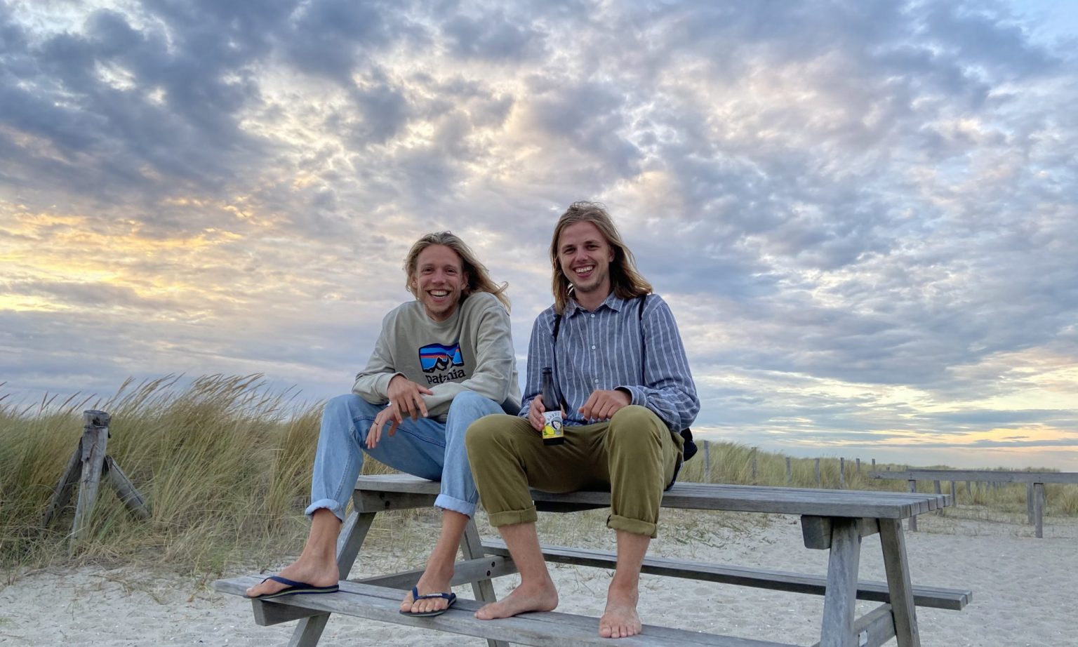 Twee jongeren zittend op een houten bankje in de duinen