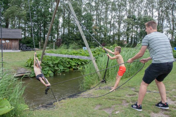 Een volwassene met twee kinderen met touwen over een sloot