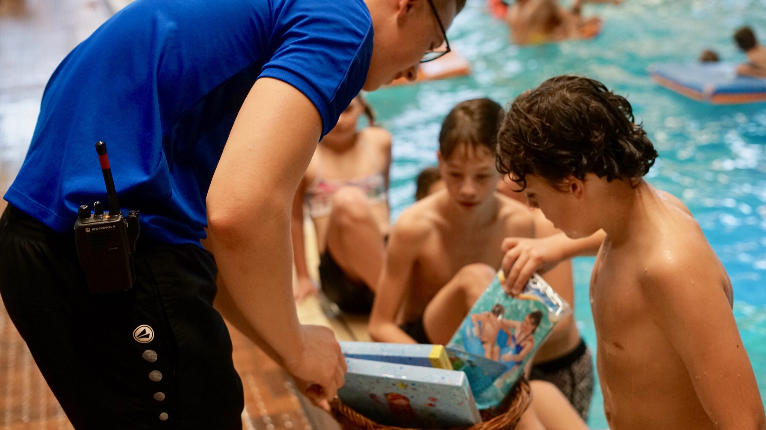 Kinderen in zwembad, badmeester laat plastic speelattributen (nog in verpakking) zien