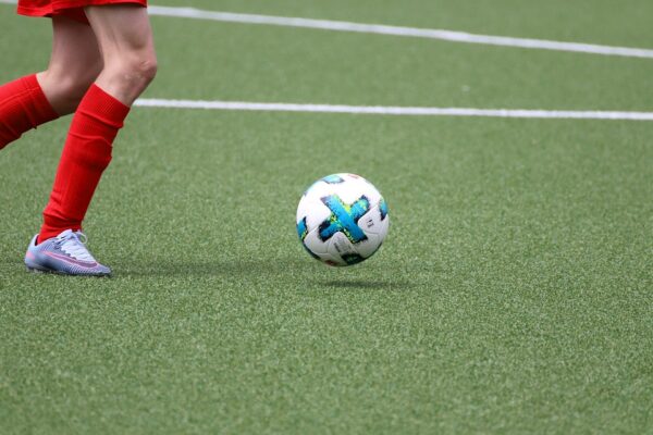 benen van kind in rood voetbaltenue met voetbal op voetbalveld