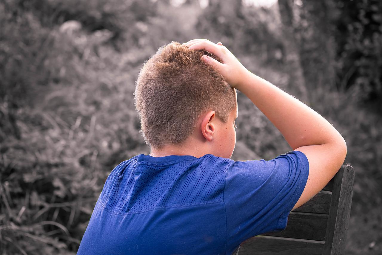 Eenzaam en droevig jongetje met helder blauw shirt tegen zwart-wit achtergrond