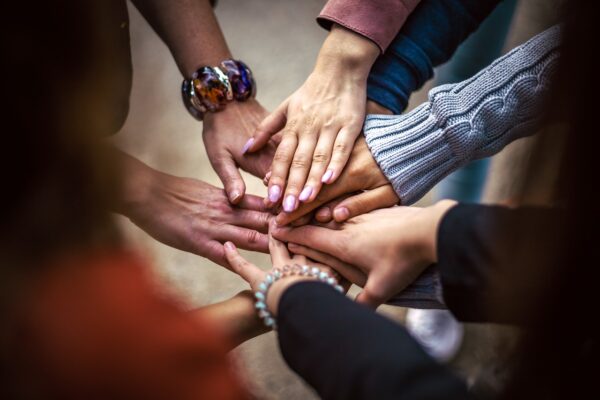 Handen van jonge mensen die in een kring staat en hun handen naar het midden van de kring op elkaar leggen