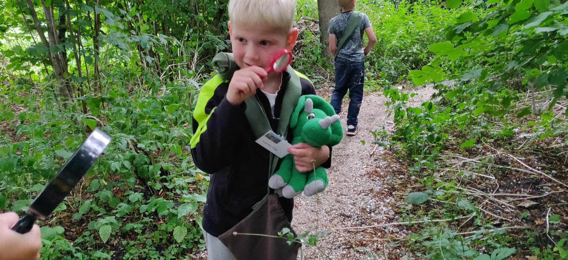 Kind met plastic loep en knuffel lopend in het bos op speurtocht