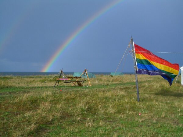 foto van regenboogvlag met op de achtergrond een echte regenboog