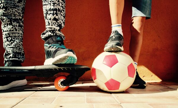 twee paar jongensbene met voetbal en skateboard