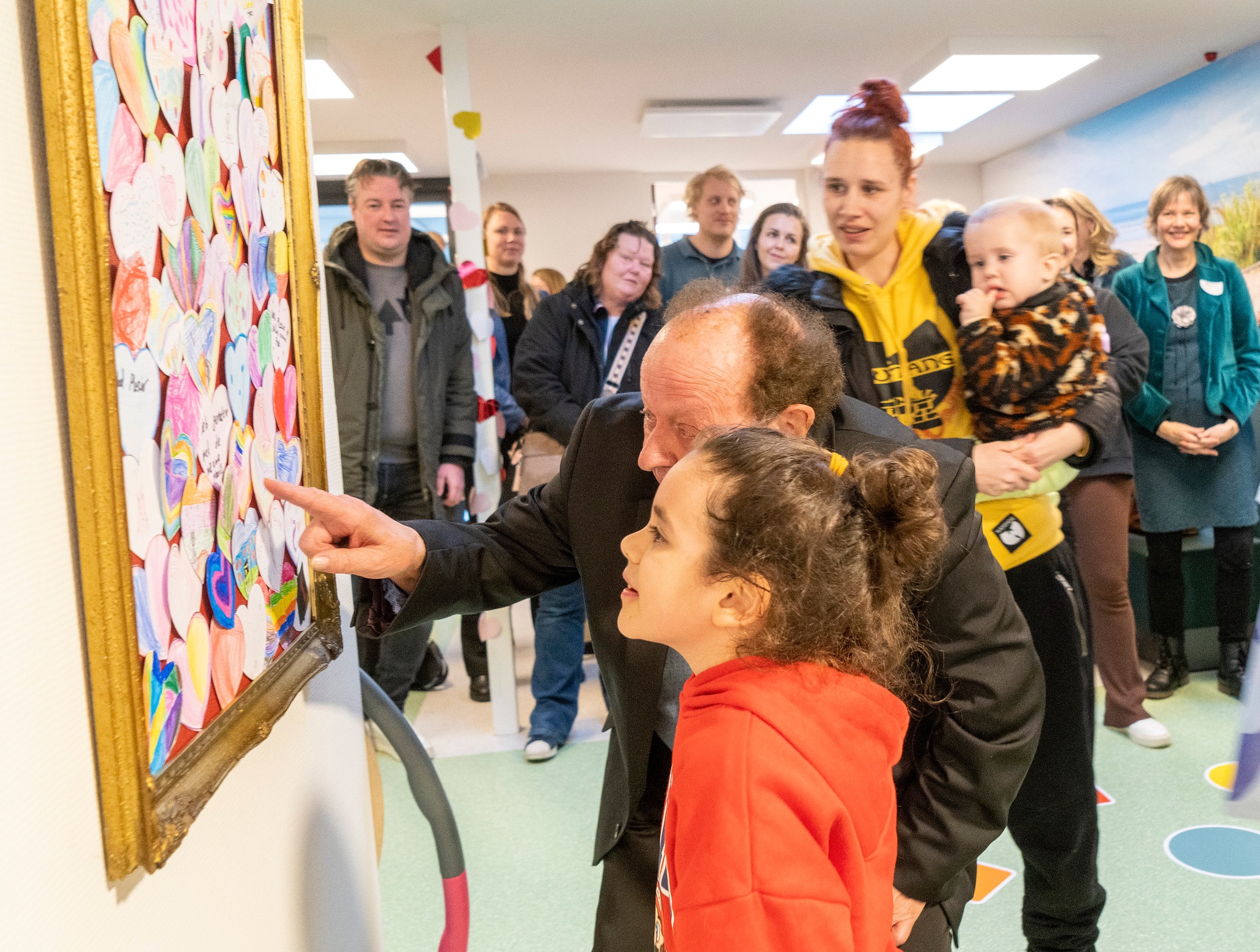 Foto van kind en wethouder Alkmaar bij de onthulling van kunstwerk gemaakt door schoolkinderen - lijst met papieren hartjes - ter gelegenheid opening nieuwe locatie CJG Zuid