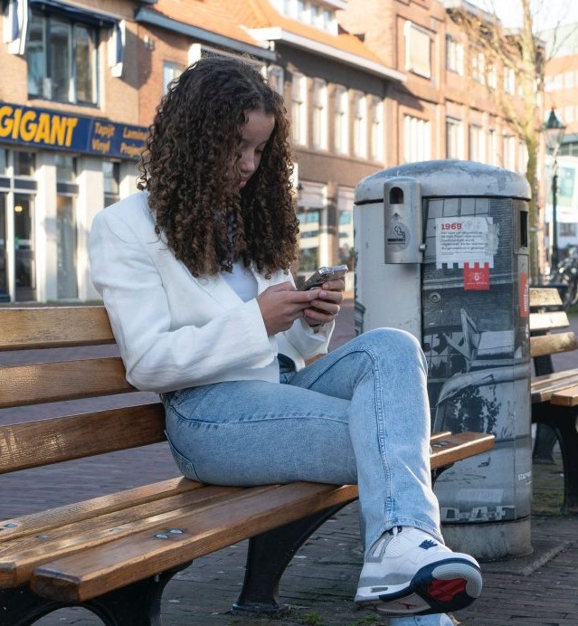 Meisje (tiener) zitten op een bankje in de stad, kijken op haar telefoon
