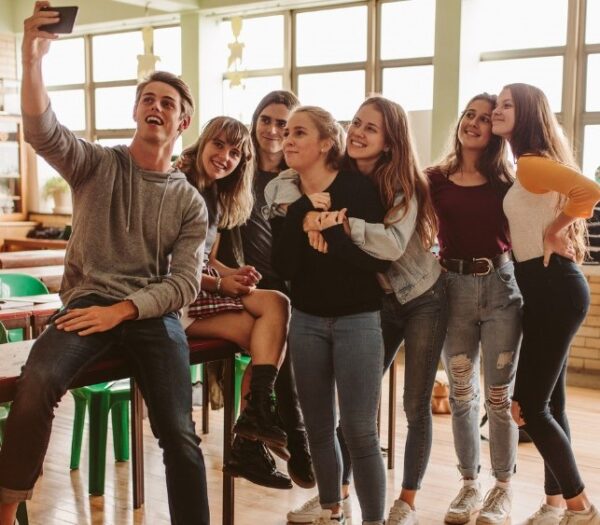 Groepje van zeven jongeren - jongens en meisjes - in een klas die een vrolijke selfie maken