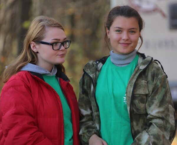 Foto van twee glimlachende tienermeisjes met boom op de achtergrond
