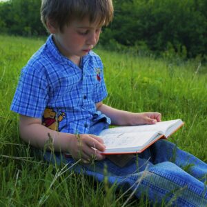 jongen zit in het gras en leest boek