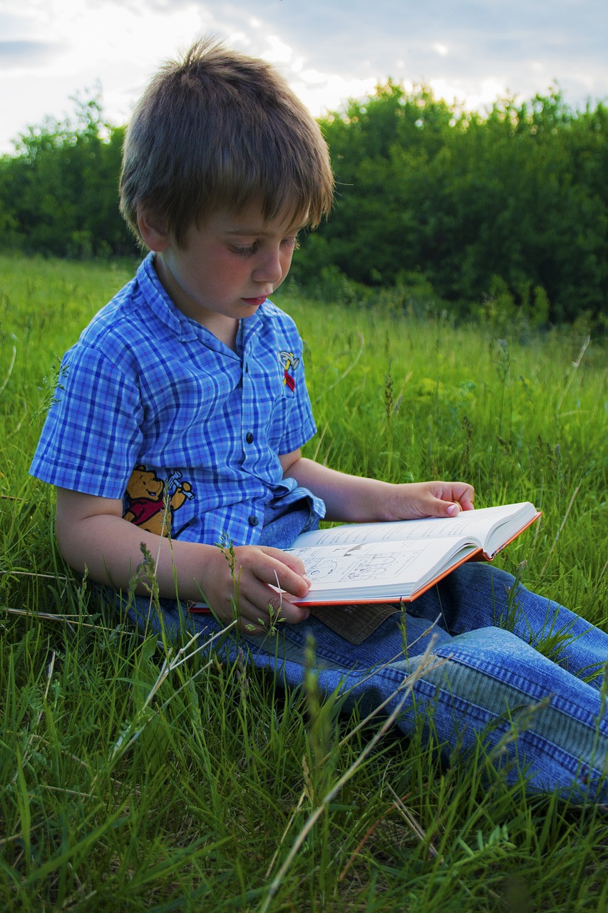 jongen zit in het gras en leest boek