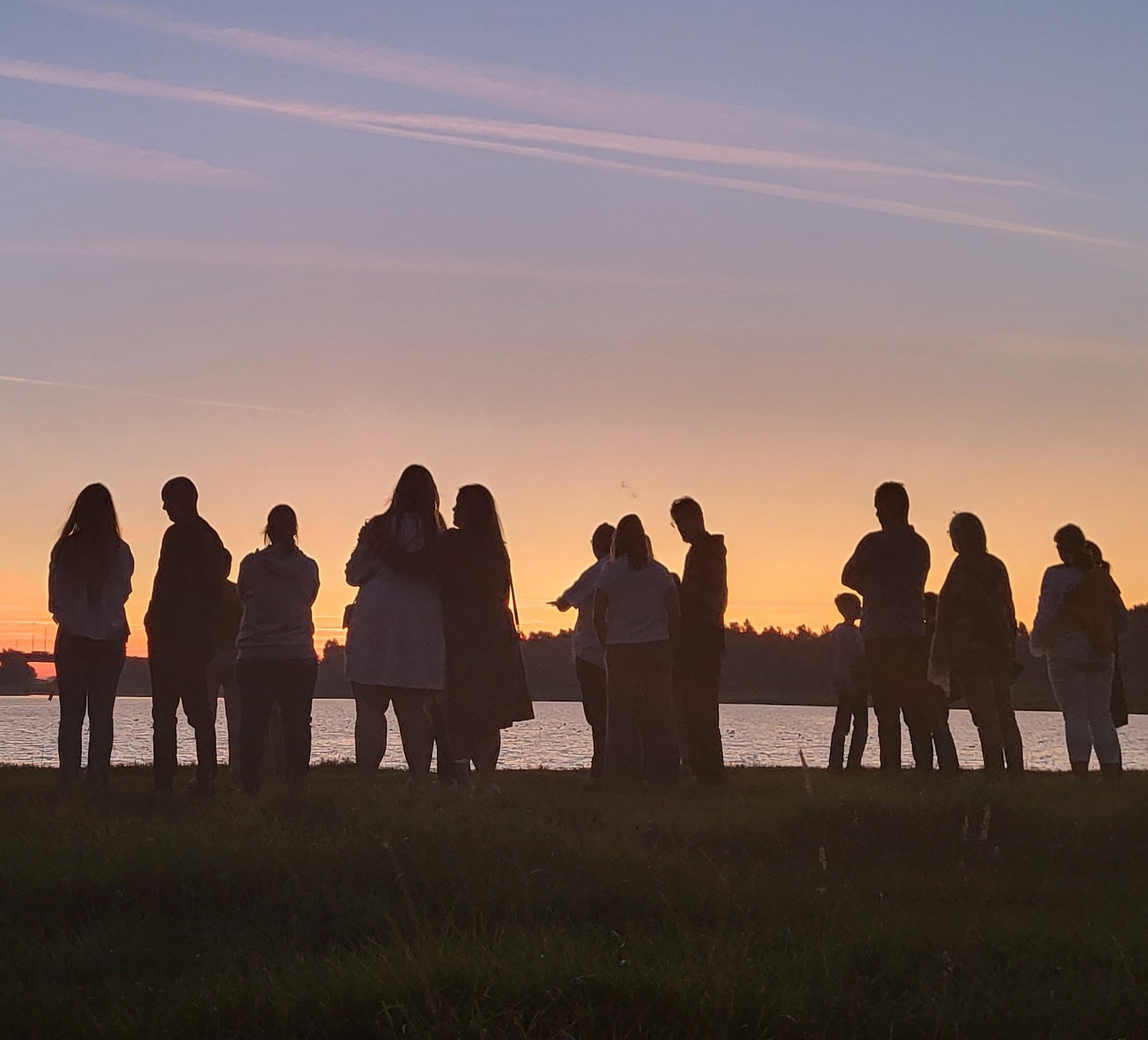 Walk-into-the-Light_rechtenvrij-voor-publicatie Foto van het silhouet van een rij mensen buiten aan de rand van een meer tijdens de schemering