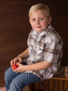 Foto van jongen in de basisschoolleeftijd in geruit overhemd en spijkerbroek zittend met een appel in de hand kind naar gezonder gewicht campagne
