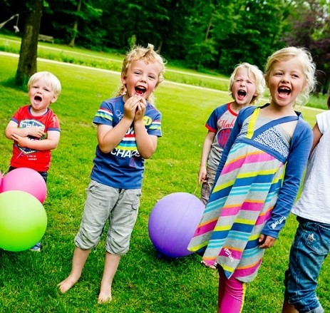 5 kinderen in kleurige kleding spelend op een grasveld met ballen en ballonnen