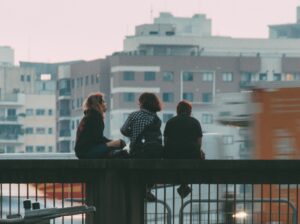 Drie jongeren zitten op een hek in een stad tegenover een paar flatgebouwen