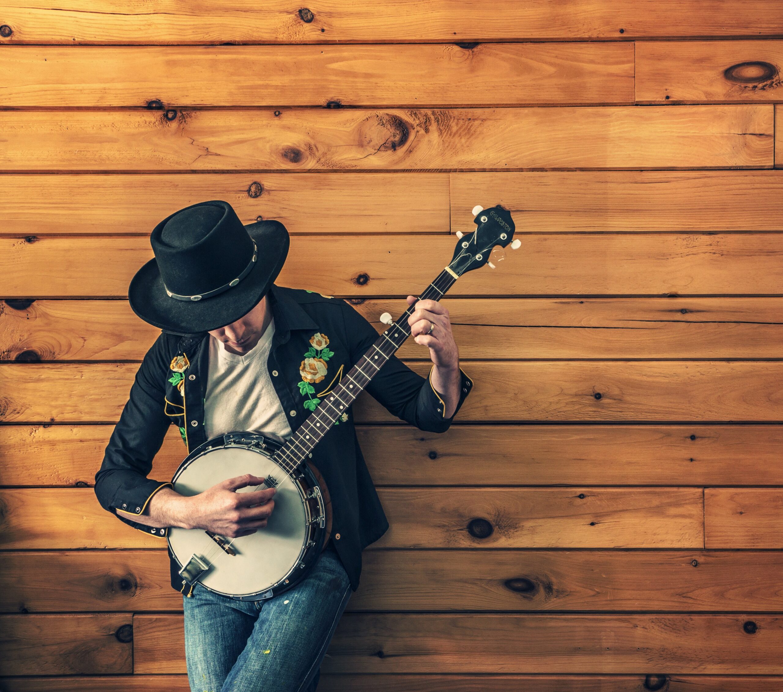 jongen-jongere met hoed op die een banjo bespeelt tegen een muur van houten planken