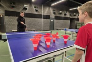 Kind dat aan een soort tafeltennisspel bezig is in een sportzaal met een begeleider